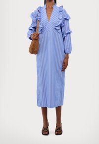 Blårandig klänning med volangärmar, V-ringning, midilängd, kombinerad med en brun mockaväska och svarta sandaler med remmar.