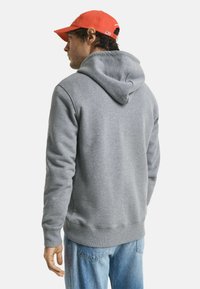 Sweat à capuche gris en mélange de coton, avec une poche kangourou, un ourlet côtelé et des poignets, porté avec un jean bleu clair.
