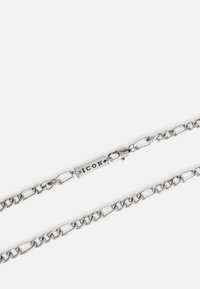 Sudraba ķēdīte, kas sastāv no ovālā formas posmiem, ar aizdares mehānismu un taisnstūrveida piekariņu, uz kura ir iegravēts "ICON". Gluda virsma un pulēts apdare.