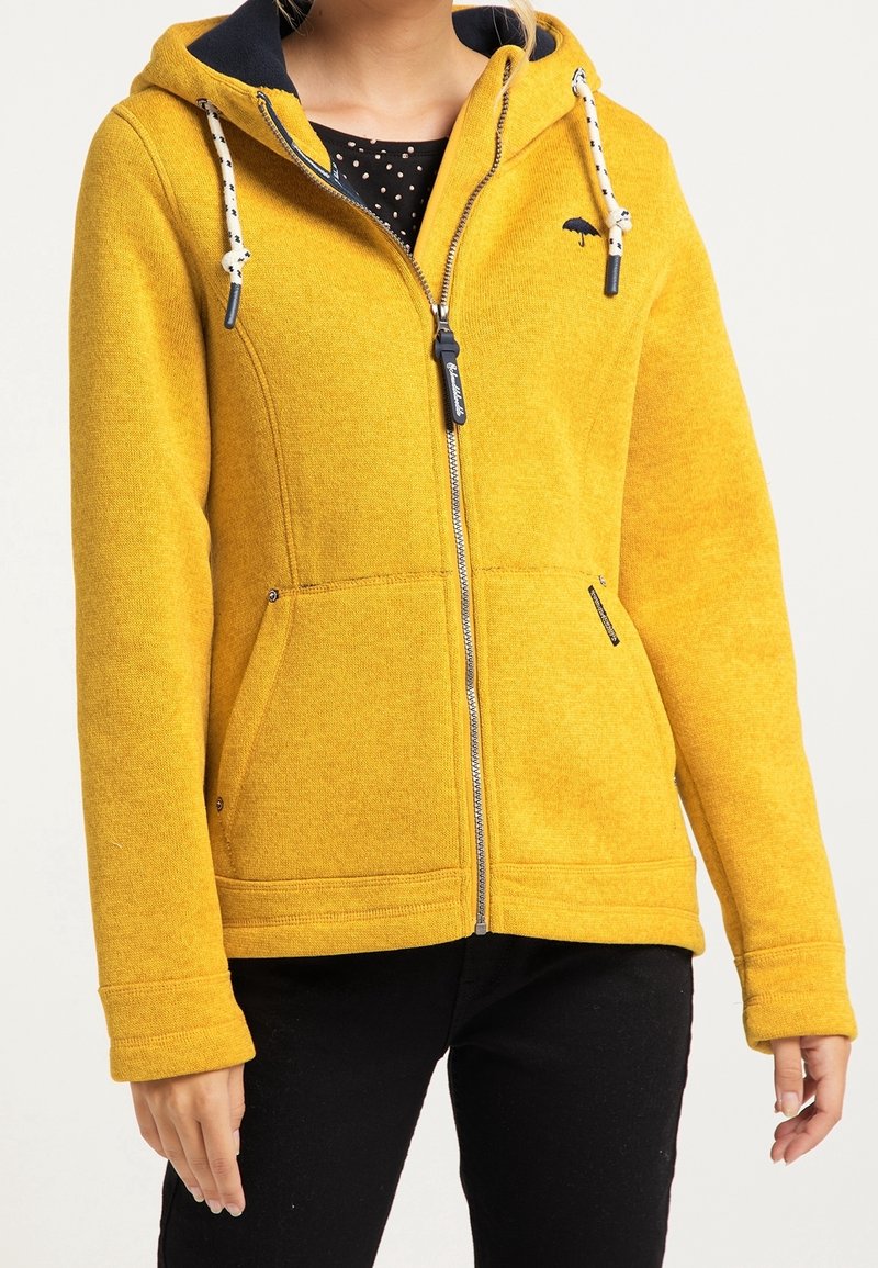 Gelbe Fleecejacke mit Reißverschluss, zwei Taschen, verstellbarer Kapuze und marineblauer Fütterung. Verfügt über weiße Kordeln und ein kleines Logo.