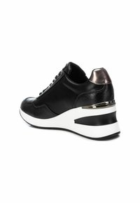 Sneaker nera con finitura testurizzata, dotata di un accento metallico sul tallone e suola a zeppa bianca. Lacci e cuciture visibili.