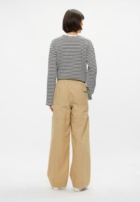 Μαύρη και λευκή ριγέ μπλούζα με μακριά μανίκια, συνδυασμένη με άνετα, μπεζ cargo παντελόνια. Διαθέτει ελαστική μέση και τσέπες με μπαλώματα.