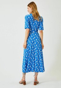 Blå blommig midiklänning med korta ärmar, åtsittande midja och flödande kjol. Har vita blommönster och kompletteras med beige klacksandaler.