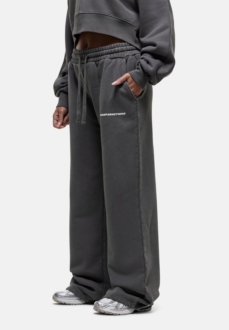 Donkergrijze sweatpants met een losse pasvorm, elastische tailleband en zijzakken. Heeft witte tekst "GOODFORNOTHING" op het been.