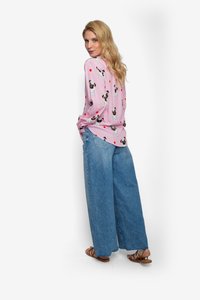 Roze shirt met lange mouwen met printjes van honden en rode hartjes, gecombineerd met wijde blauwe spijkerbroeken. Sandalen maken de outfit compleet.