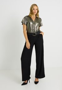 Haut court en argent métallique à col en V profond, associé à un pantalon en tissu texturé noir à jambes larges et une large ceinture noire avec boucle circulaire.