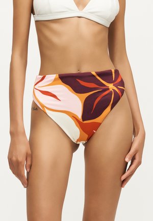 Kobieta w majtkach bikini z wysokim stanem z dużymi abstrakcyjnymi kwiatowymi wzorami w kolorach pomarańczowym, burgundowym, białym i różowym.