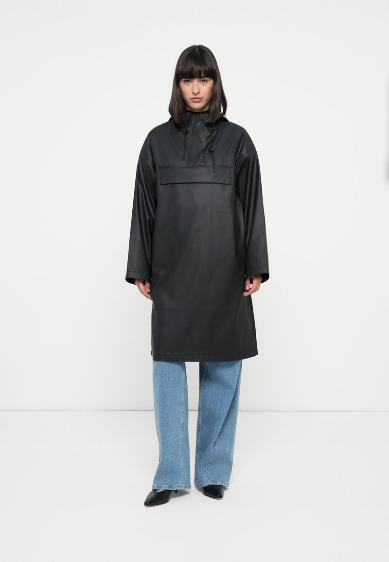 Black waterproof parka with a high neck, front pocket, and drawstring. Features long sleeves and a relaxed, knee-length silhouette.