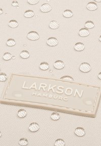 Textile résistant à l'eau en beige clair avec des gouttes en relief. Présente une étiquette logo de couleur crème emboutie avec "LARKSON HAMBURG".