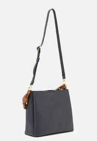 Ciemnoniebieska skórzana torebka o wyraźnej, usztywnionej formie. Posiada odpinany ciemny pasek i jasnobrązowe aplikacje. Na pasku widoczne złote okucia.