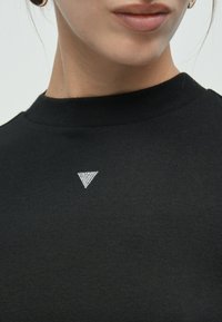 T-shirt nera in cotone con scollo alto. Presenta un piccolo disegno a triangolo di strass argentati sul davanti. Texture morbida, vestibilità casual.