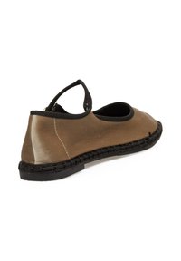 Zapato marrón de ante tipo slip-on con punta redondeada, banda elástica negra y detalle de suela trenzada. Textura suave con un acabado mate y blando.
