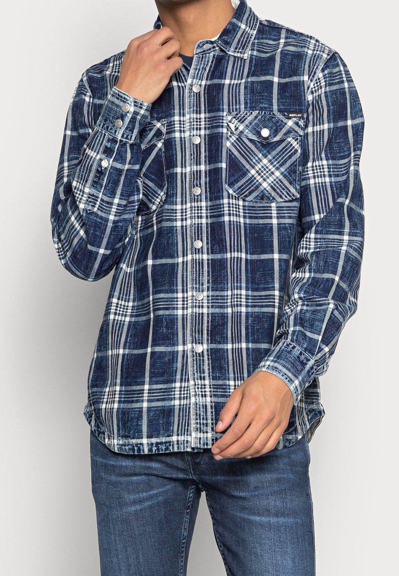 Camicia a quadri blu e bianca in cotone, con colletto a bottoni, taschino sul petto e maniche lunghe con polsini a bottone.