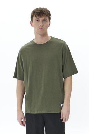 Camiseta de algodón verde oliva con corte relajado, cuello redondo y mangas cortas. Presenta una pequeña etiqueta en el dobladillo y una textura suave.