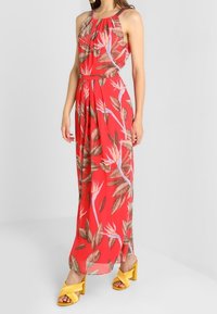 Maxikjole i rød stof med blomstermotiv, der har pink og grønne blade. Sættes sammen med gule højhælede sko.