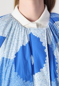 Vestimenta azul com um padrão de manchas brancas e azuis claras, com um colarinho branco e uma textura franzida à volta do decote.