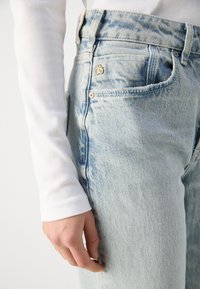 Lys blå denim jeans med et subtilt falmet mønster, fem-lomme design, metallisk hardware og en teksturert finish. Kombinert med en hvit ribbet topp.