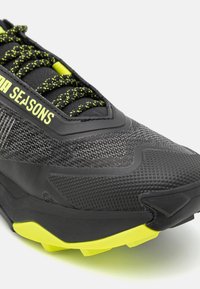 Scarpa da ginnastica nera con tomaia in mesh testurizzato, accenti gialli a contrasto e lacci con un motivo maculato. Suola resistente con trazione.