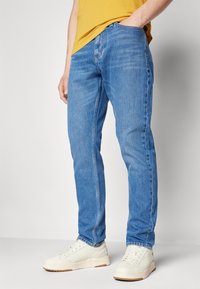 Blå denimjeans med en slim-fit design, som har en standard femficks-layout och en subtilt blekt textur, i kombination med vita sneakers.