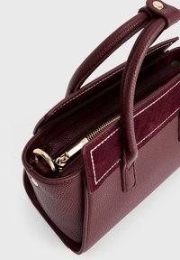 Borsa in pelle bordeaux profondo con doppi manici superiori, pannello frontale in suede, cuciture bianche e dettagli in oro sulla zip e sulle parti metalliche.