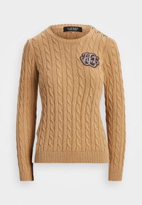 Kabelstickad tröja i beige med rund halsringning, ribbade ärmmuddar och nederkant. Har dekorativa knappar på axeln och en broderad logotyp.