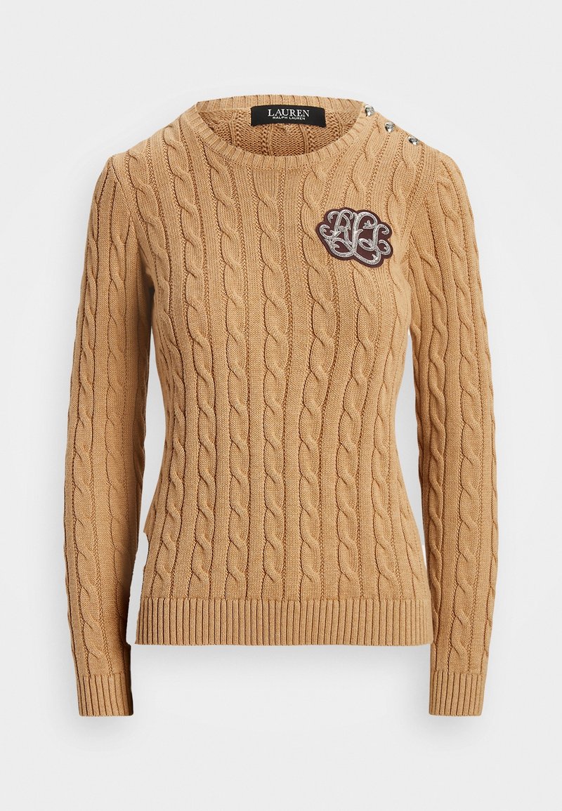 Kabelstickad tröja i beige med rund halsringning, ribbade ärmmuddar och nederkant. Har dekorativa knappar på axeln och en broderad logotyp.