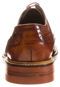 Chaussure en cuir marron avec détails brogue, bout rond et talon en bois empilé. Texture lisse et couture contrastante.