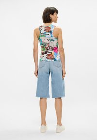 Πολύχρωμο αμάνικο μπλουζάκι με γραφικό σχέδιο, συνδυασμένο με ανοιχτό μπλε τζιν κολάν. Το αμάνικο έχει εφαρμοστή σχεδίαση και φαρδιές τιράντες.