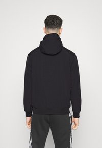 Black hooded jacket with a smooth texture, elastic cuffs, and waistband; designed with a minimalist style and no visible logos or accents.