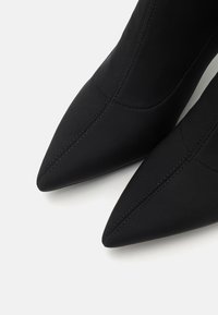 Black pointed-toe ankle boots made from smooth fabric featuring seam detailing and a fitted design. The heels are modestly tall.