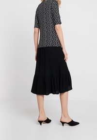 Vestido negro con un dobladillo acampanado y volantes, con un cuerpo ajustado de estampado floral. El material parece ligero y suave. Mules negros completan el look.