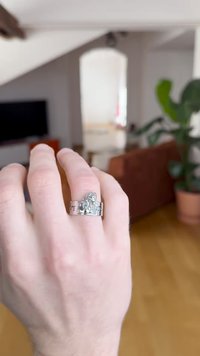 Strieborný prsteň s detailným dizajnom karikatúrnej postavičky, s lešteným povrchom a širokým pásikom. Ruka zobrazená na rozostrenom vnútornom pozadí.