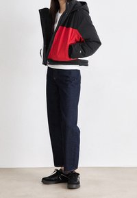 Prošívaná bunda v černé a červené barvě s kapucí, zapínáním na zip a bočními kapsami. Doplněná tmavě modrými džíny s rovnými nohavicemi a černými teniskami.