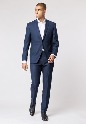 Navy blue suit with a structured design, single-breasted jacket, notch lapels, and two buttons; paired with a white dress shirt and black shoes.