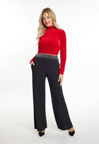 Rotes Samtoberteil mit mock Turtle Neck und glitzernden Akzenten, kombiniert mit weiten schwarzen Hosen mit einem bestickten Taillenbund.