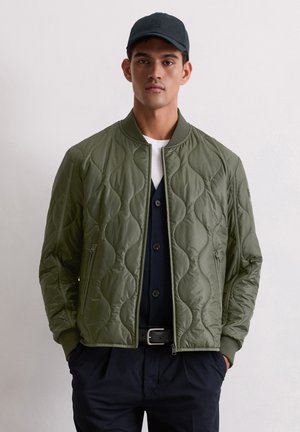 Olijfgroene gevoerde bomberjack met een ritssluiting aan de voorkant, geribbelde kraag en zakken aan de zijkant, gelaagd over een marineblauwe blouse met knopen.