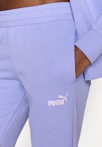 Φόρμες από μαλακό φλις σε ανοιχτό μωβ χρώμα με ελαστική μέση, πλαϊνές τσέπες και λευκό λογότυπο Puma στο κάτω μέρος του ποδιού. Λείο υφή.