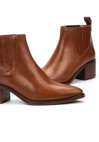 Bottines en cuir marron avec un bout pointu, des panneaux latéraux élastiques et un talon empilé. Texture lisse avec un design épuré.