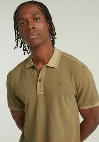 Polo shirt verde oliva con una texture morbida, colletto a contrasto e due bottoni. Presenta un logo discreto sul petto.