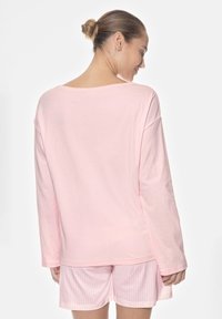 Maglietta rosa a maniche lunghe con scollatura ampia abbinata a pantaloni corti a righe rosa. Materiale in cotone morbido, vestibilità comoda e design semplice.