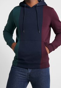 Sudadera con capucha que presenta bloques de color en azul marino, verde y burdeos, material de mezcla de algodón, bolsillo tipo canguro y capucha ajustable con cordón.