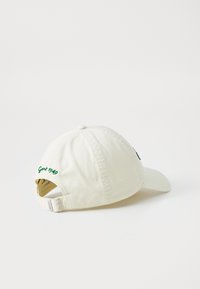 White cotton baseball cap with a curved brim, featuring green embroidered text "Gant 1949" and a metal adjustable strap at the back.