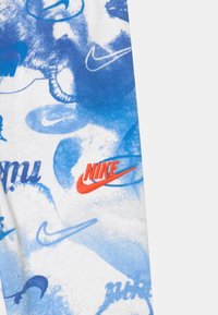 Modrý a bílý vzorovaný textil s různými logy Nike v různých odstínech modré a jedním v červené. Měkká textura s abstraktními designovými prvky.
