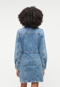 Τζιν φόρεμα μ�ε μακριά μανίκια, μπλε πλύσιμο, εφαρμοστό μέση με ζώνη και δύο πίσω τσέπες. Διαθέτει κλασική ραφή και δομημένο σχεδιασμό.