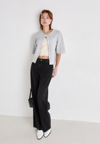 Lysegrå, teksturert strikkegenser med korte ermer, kombinert med en beige cropped topp og svarte vide bukser. Hvite spisse ankelstøvler.