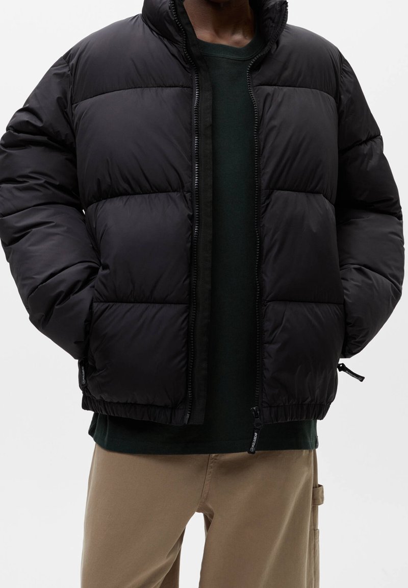 Sort puffjakke med quiltet design, høj krave og lynlås. Har justerbar kant og synlige syningsdetaljer.