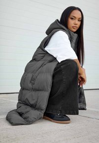 Chaleco acolchado con capucha en gris oscuro, con secciones acolchonadas, llevado sobre una camisa blanca y una falda de mezclilla negra, acompañado de zapatillas negras.