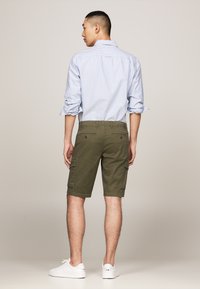 Shorts cargos vert olive avec poches latérales, associés à une chemise à rayures bleu clair à boutons et manches retroussées, portés avec des baskets blanches.