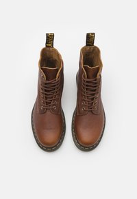 Bottes chelsea en cuir marron avec une finition texturée, semelles en caoutchouc noires, surpiqûres jaunes et languettes noires en haut.