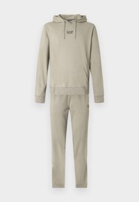 Világos bézs kapucnis pulóver és hozzáillő melegítőnadrágok az EA7 Emporio Armani logójával a mellkason és a bal combon.